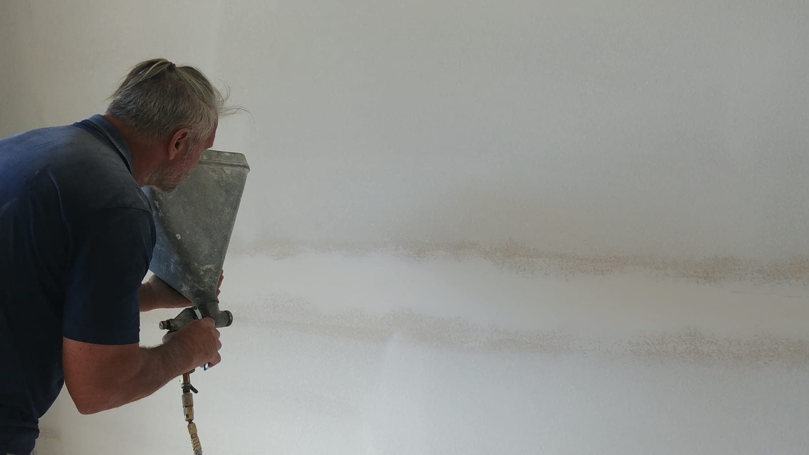 Contractors On Call worker spraying drywall texture with a hopper gun