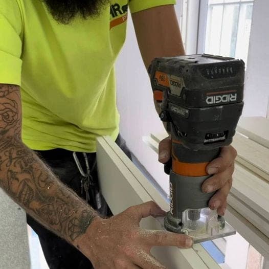 Close-up of a tattooed carpenter running a Ridgid router along a piece of trim stock