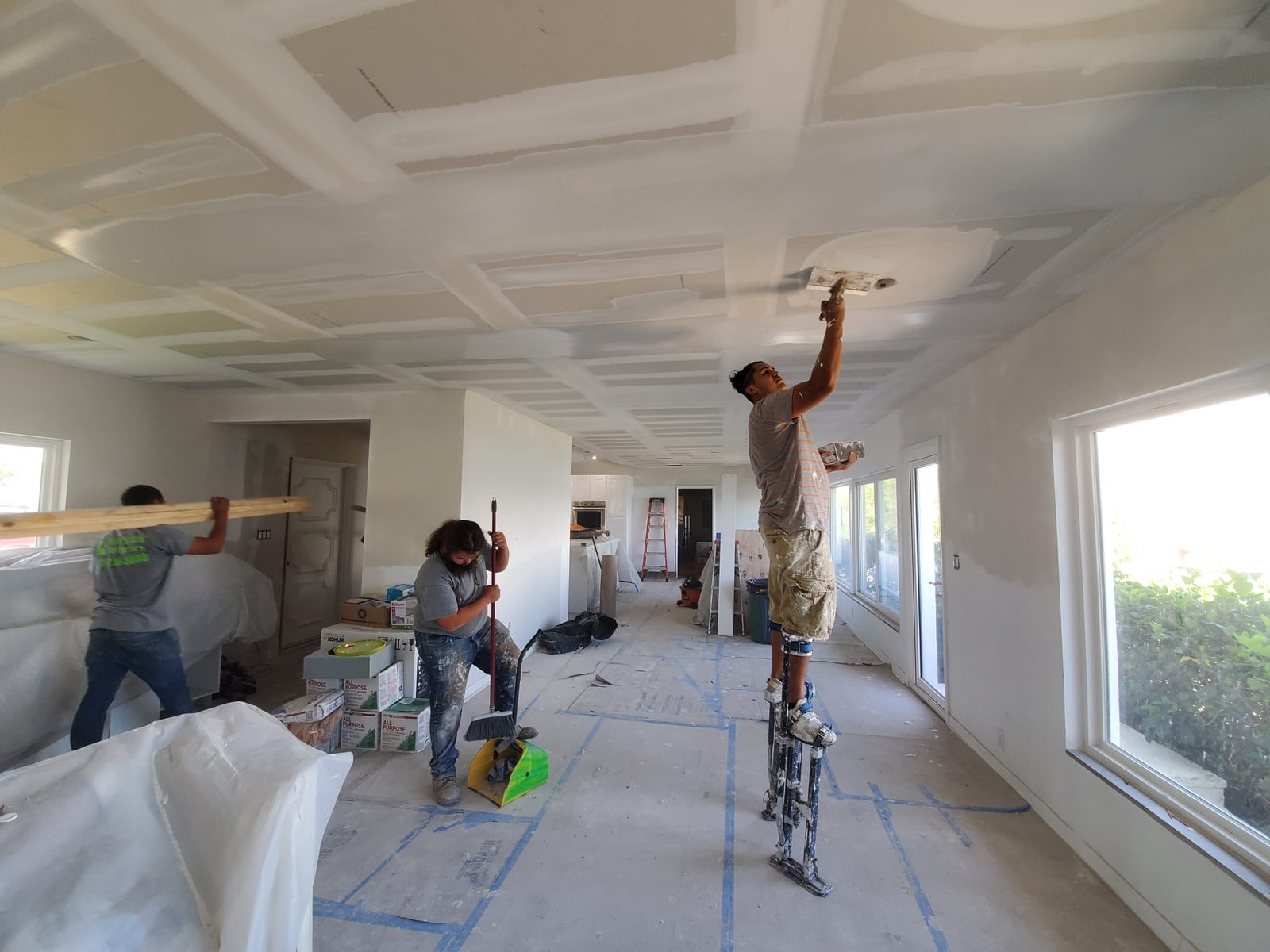 Contractors On Call crew skim-coating a ceiling on stilts inside a St. Petersburg home